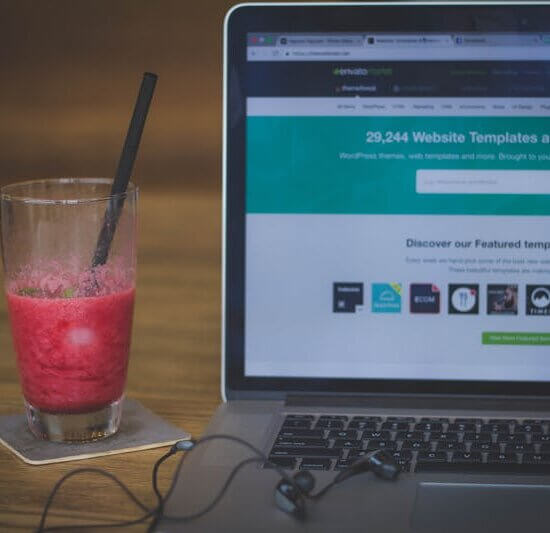 A fruit shake on a desk next to a laptop displaying a website, blending work and refreshment.