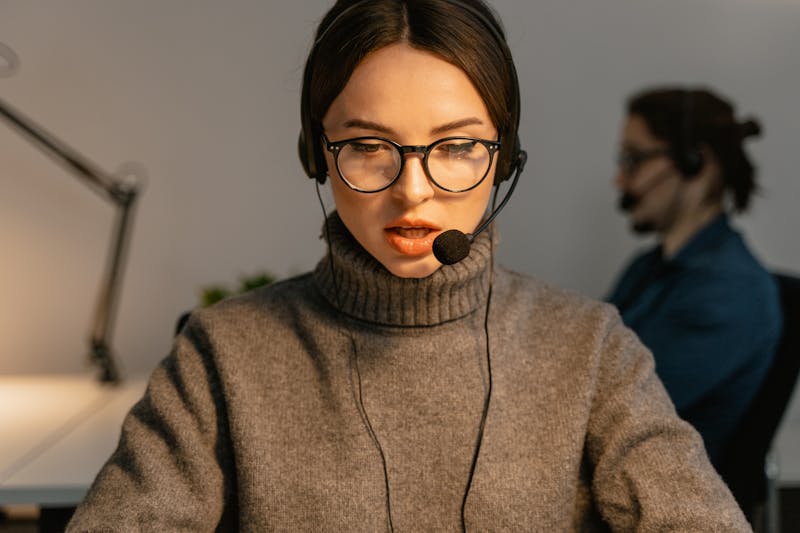 A call center agent wearing glasses and a headset, working in an office.