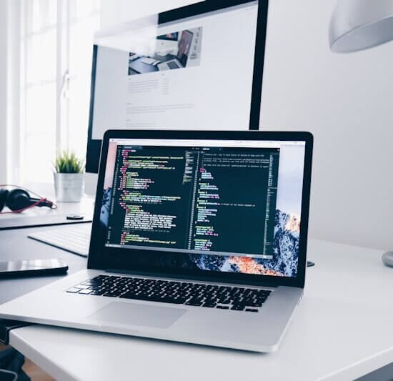 A MacBook with lines of code on its screen on a busy desk